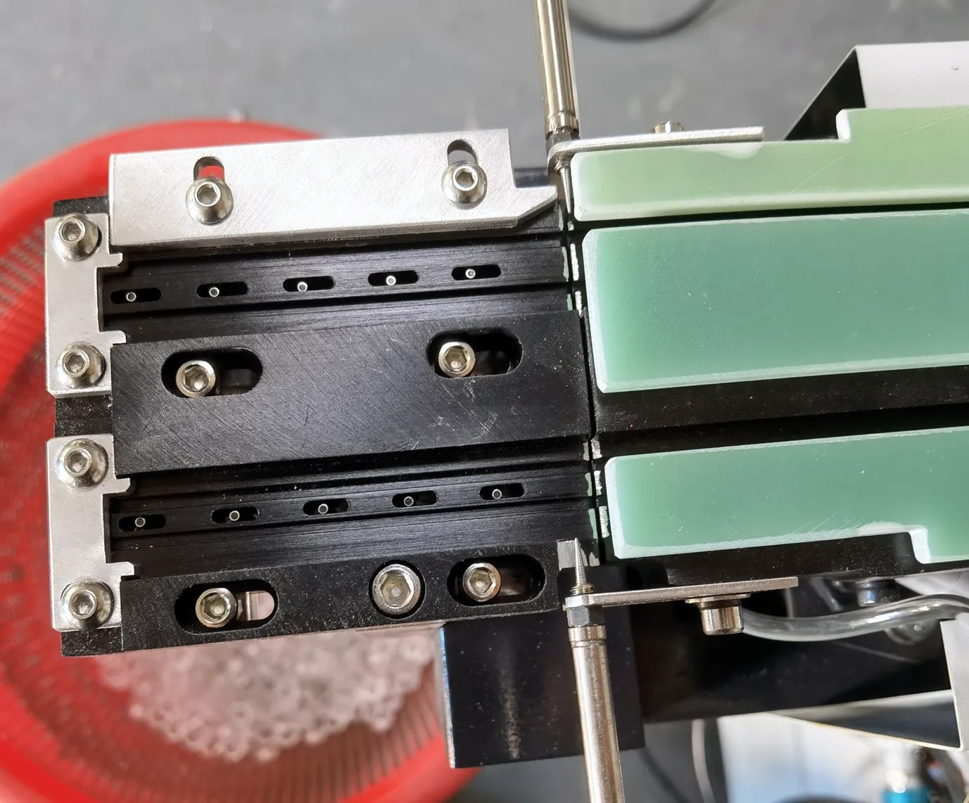 Close-up of the DPS-2 pickup platform: black linear track rails with lens feet in the slots and green guide plates at the pickup end