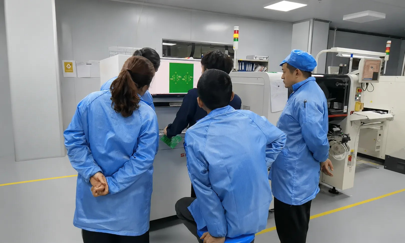 Operarios con ropa antiestática ESD recibiendo formación práctica junto a una impresora de pasta de soldadura en la planta