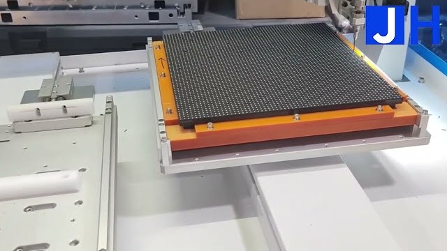 Automatic screw tightening machine with an LED module fixtured on an orange carrier on the worktable, photographed from the JHIMS official YouTube channel video